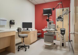 Compact exam rooms include a sink/work counter, exam chair, slit lamp, and guest chair. Accent walls match Pod colors.